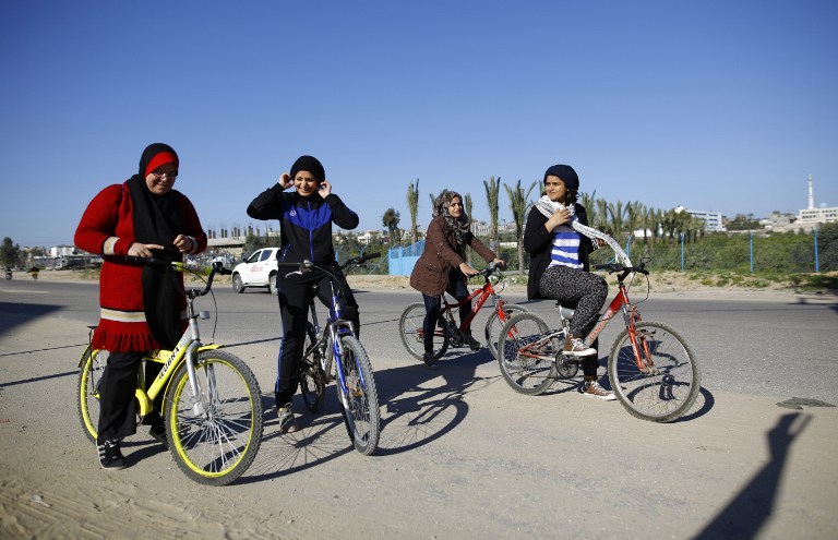 (FILES) This file photo taken on February 19, 2016 shows (from L-R) Palestinian Amneh Salman, Sarah Sleibi, Nour Sleibi and Assalah Abu Sharkh riding their bicycles on a road in Beit Hanun in the northern Gaza Strip, on February 19, 2016. The young women cycle twice a week from the north of the Gaza strip to the border with Israel and back. The women hope to encourage other women to take up sports, and challenge stereotypes.  / AFP / MOHAMMED ABED / TO GO WITH AFP STORY BY ADEL ZAANOUN